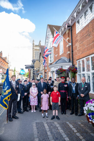Group of people standing in front of a building where the armed forces day flag is flying.