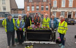 Group of people planting flowers in a large container.