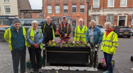 Group of people planting flowers in a large container.