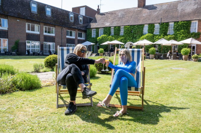 Two females sitting in deckchairs in a garden with a hotel in the background.