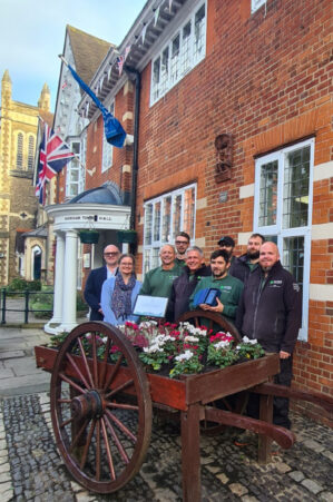 Group of people standing behind a cart planted with flowers.