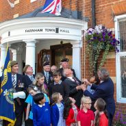 School children and group of adults looking up at a flag being raised.