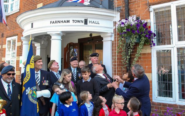 School children and group of adults looking up at a flag being raised.