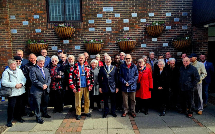 Group of people in front of a wall showing a number of commemorative plaques.