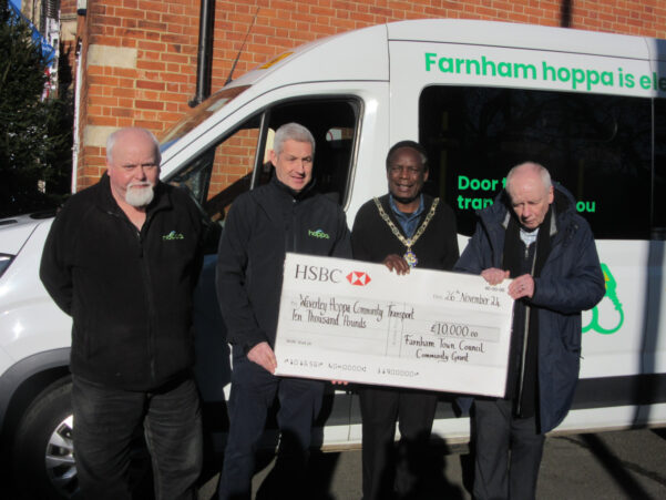 Four men standing in front of a bus holding a large cheque.