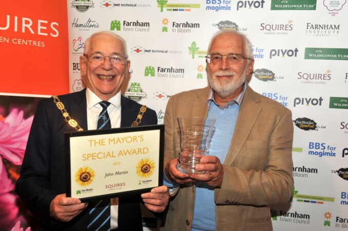 Mayor holding a certificate. Man on right of Mayor holding a glass trophy.