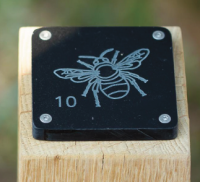 Engraving of a bee on a black tile which is mounted to the top of a wooden post.