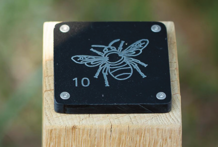 Engraving of a bee on a black tile which is mounted to the top of a wooden post.