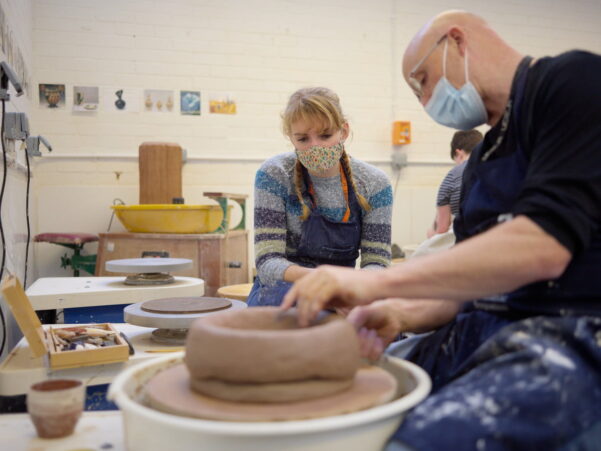 Man teaching a student how to create pottery, by example