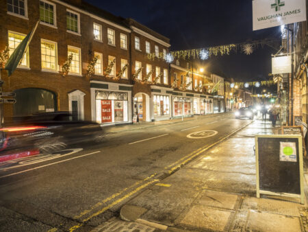 A town centre, row of Georgian buildings with a road running through it and Christmas lights