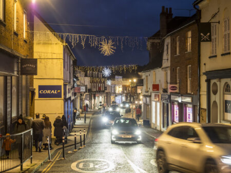 A town centre with a road running through it, decorated with hanging Christmas lights