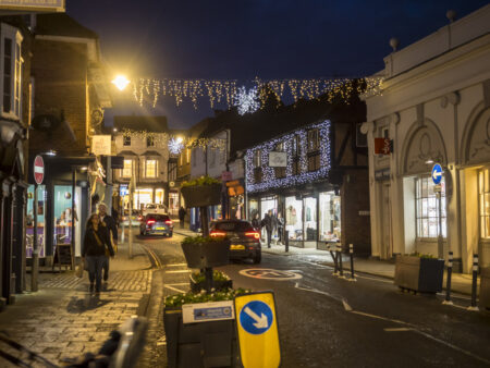 A town centre with a road running through it, decorated with hanging Christmas lights
