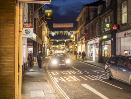 A town centre with a road running through it, decorated with hanging Christmas lights