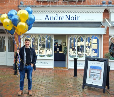 Man standing in front of a shop holding a bunch of blue and yellow balloons