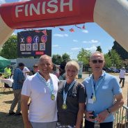 Three people standing under an inflatable 'finish' line wearing medals.
