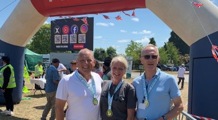 Three people standing under an inflatable 'finish' line wearing medals.
