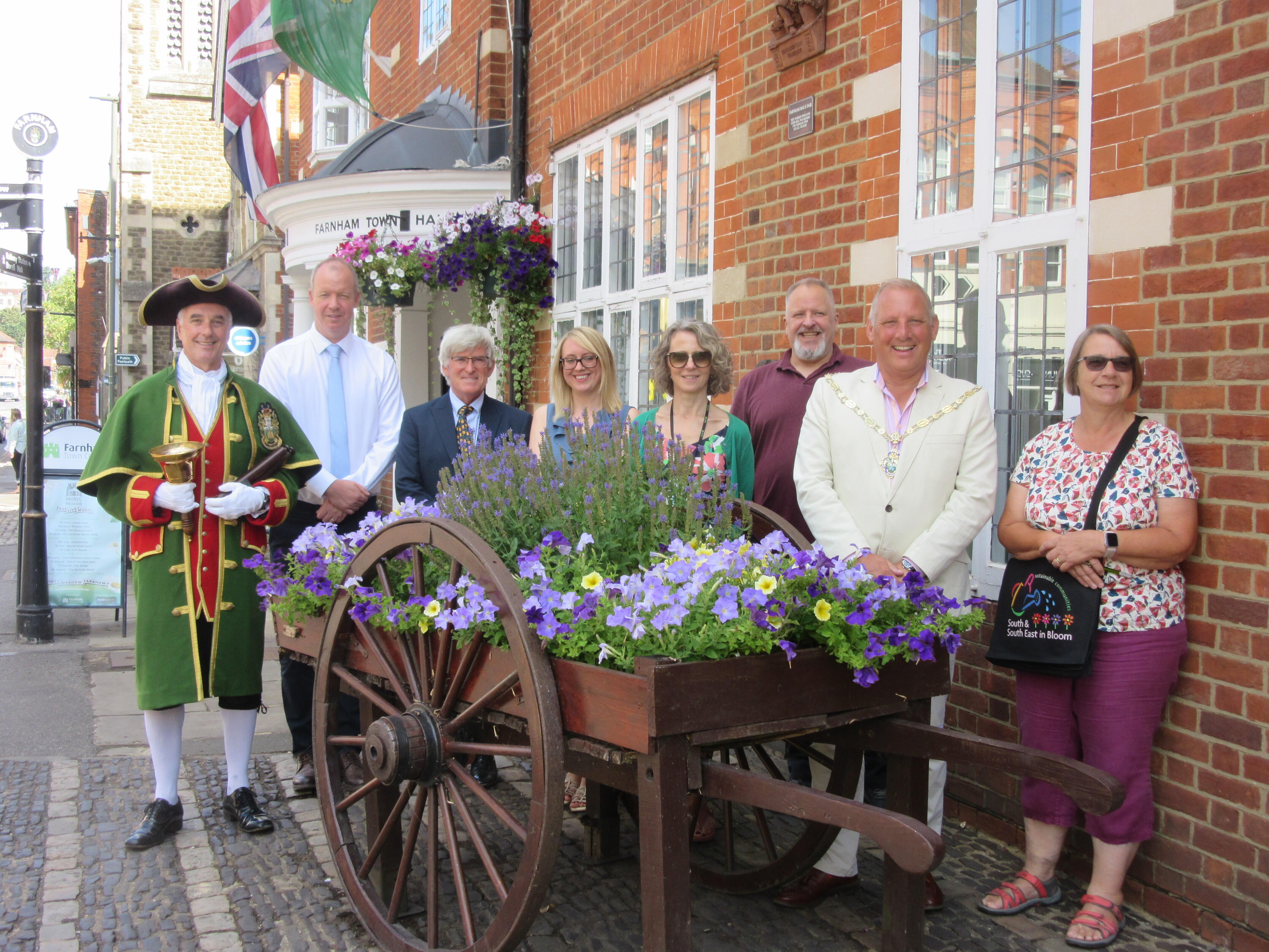 Group of people standing around a hop cart planted with flowers.