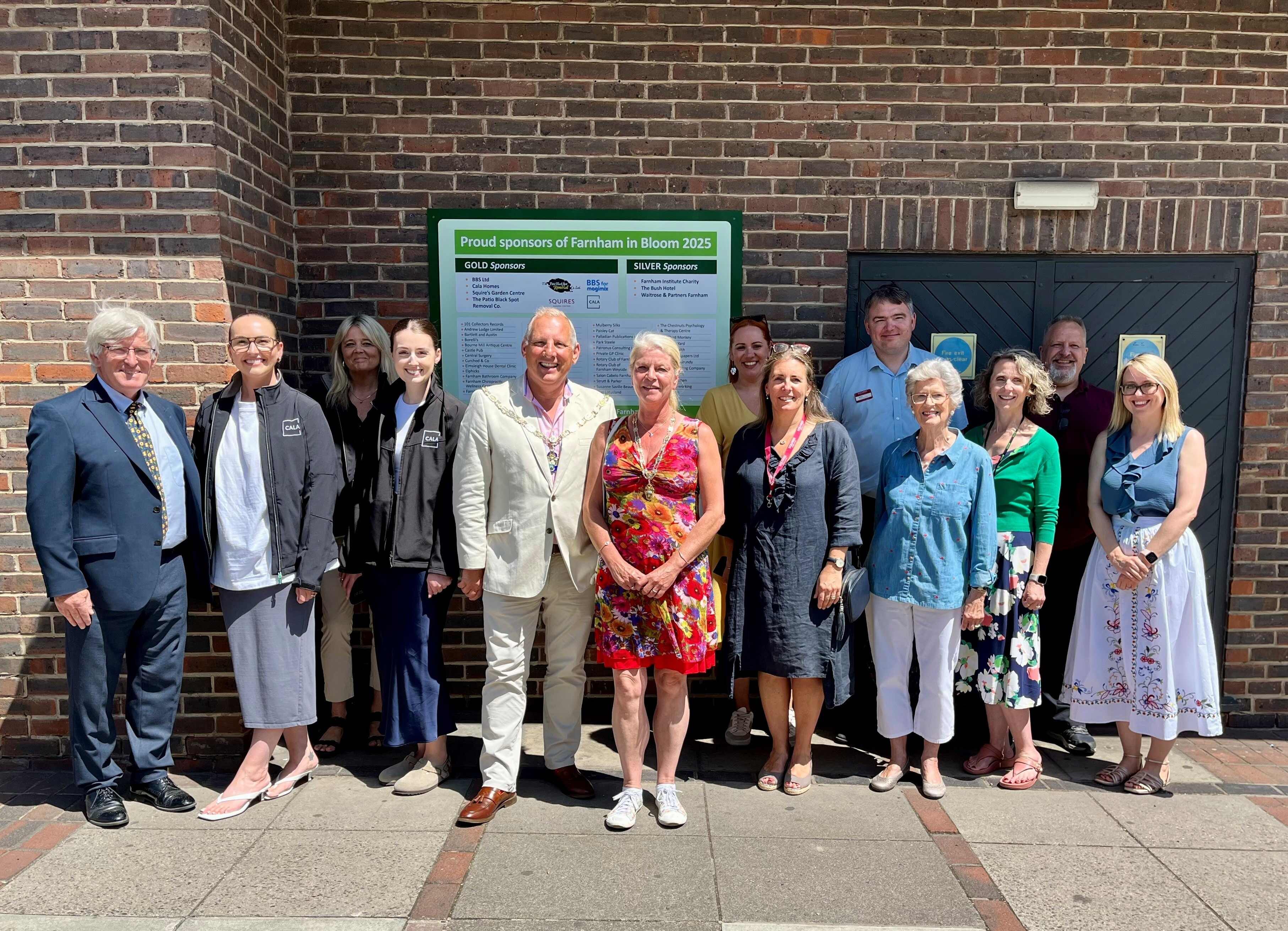 Group of people standing in front of a display board showing the sponsors of Farnham in Bloom.