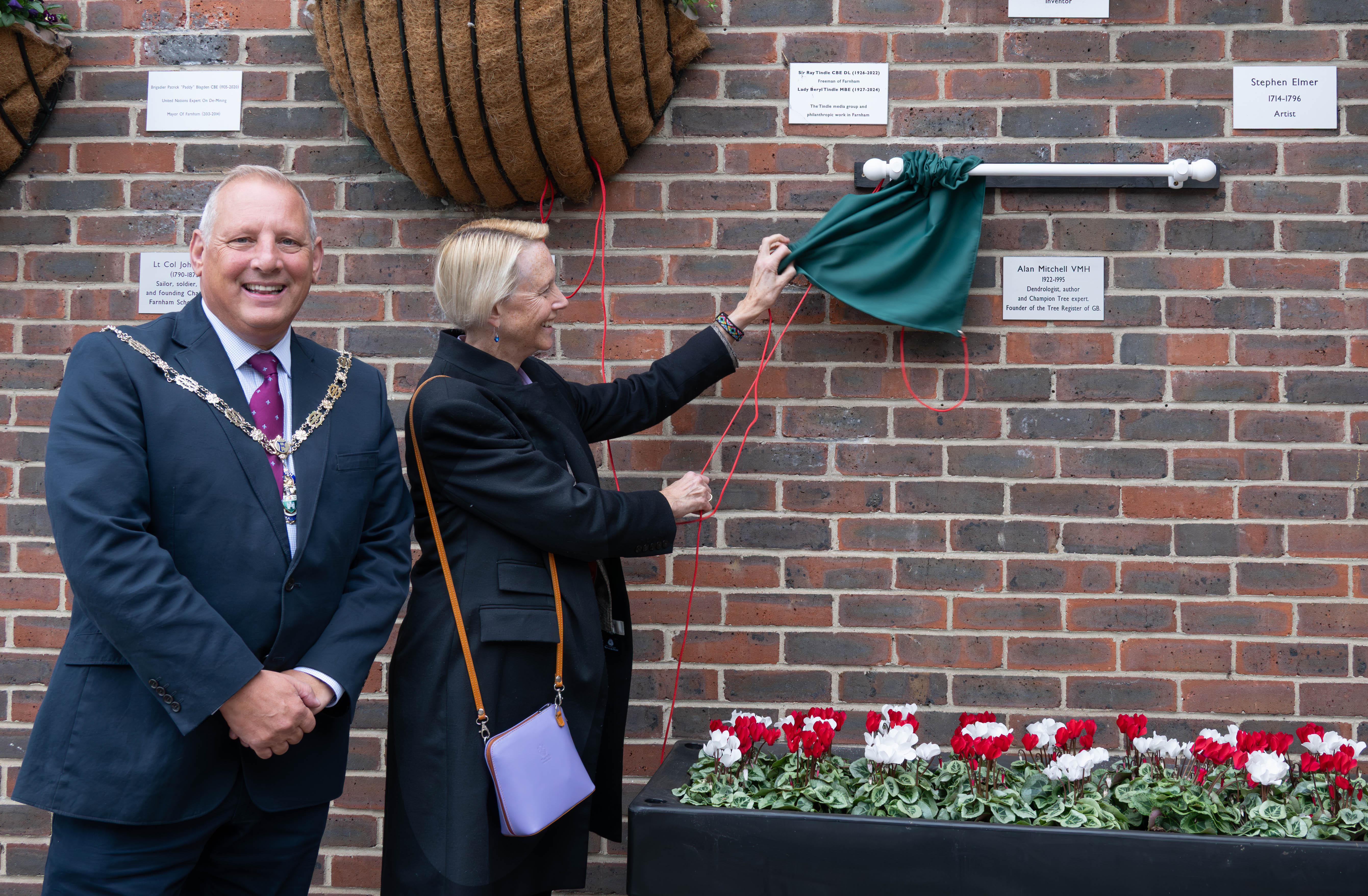 Mayor standing next to a female unveiling a silver plaque on a wall.