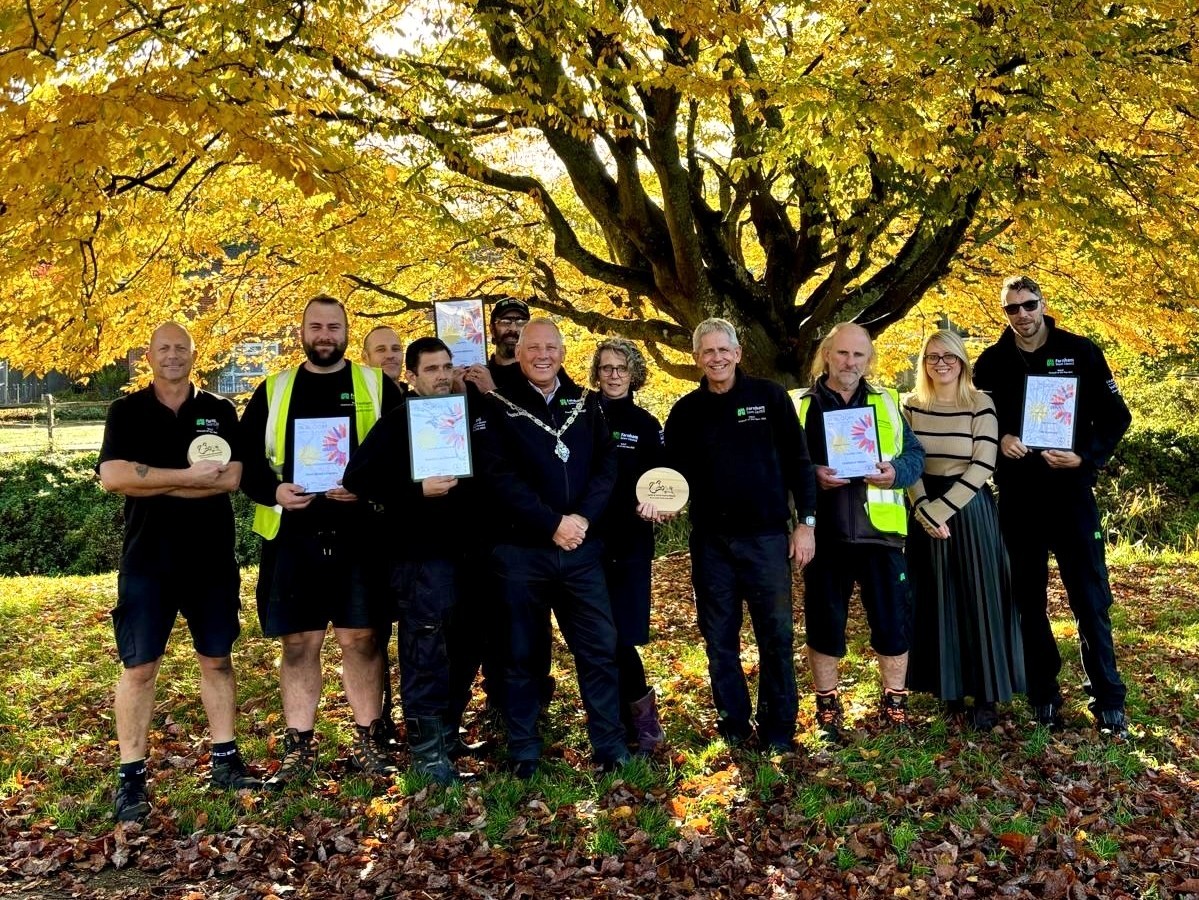 Group of people holding certificates and trophies against a backdrop of a golden leafed tree.