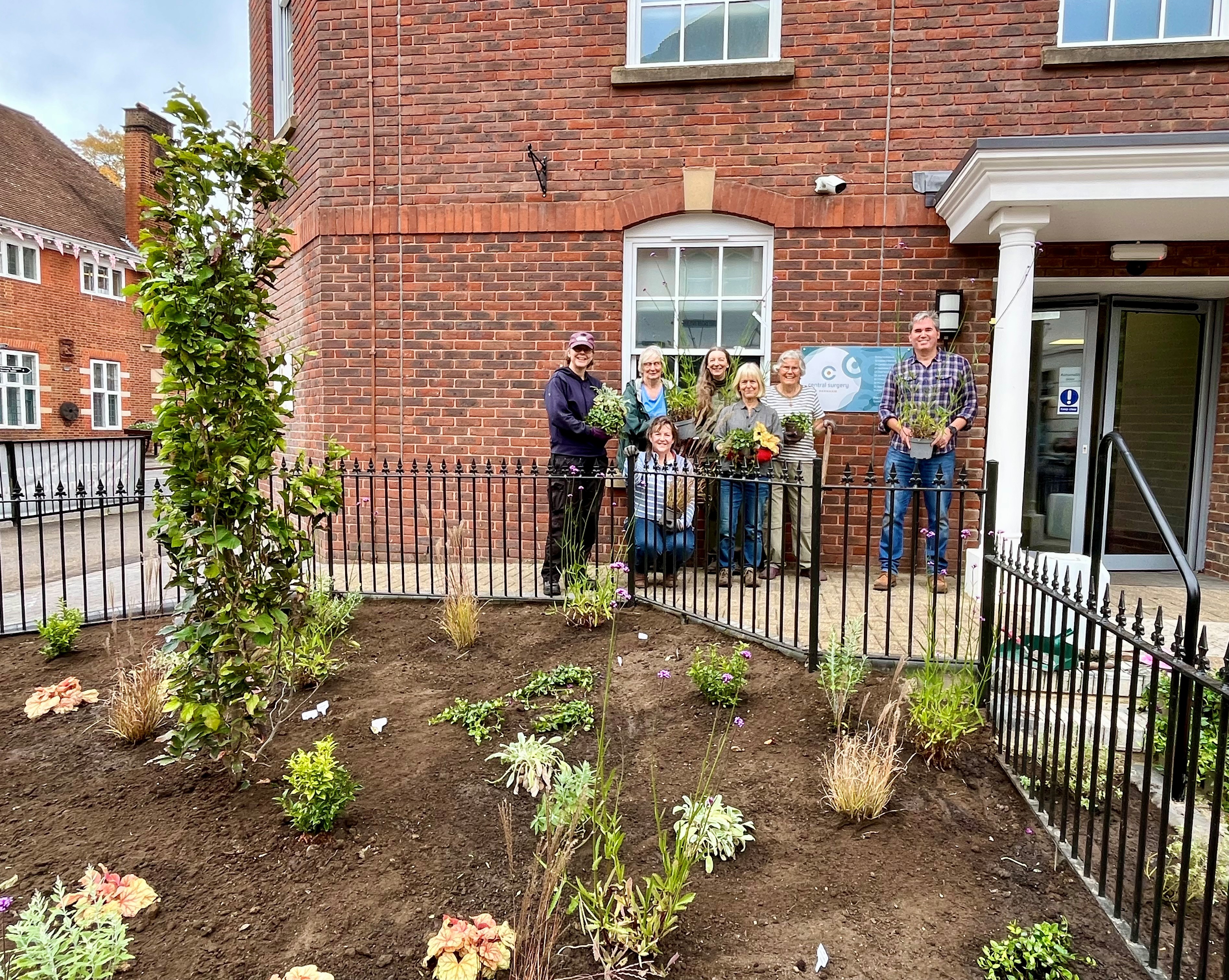 Newly planted garden in front of a building. Group of people holding plants in the background.