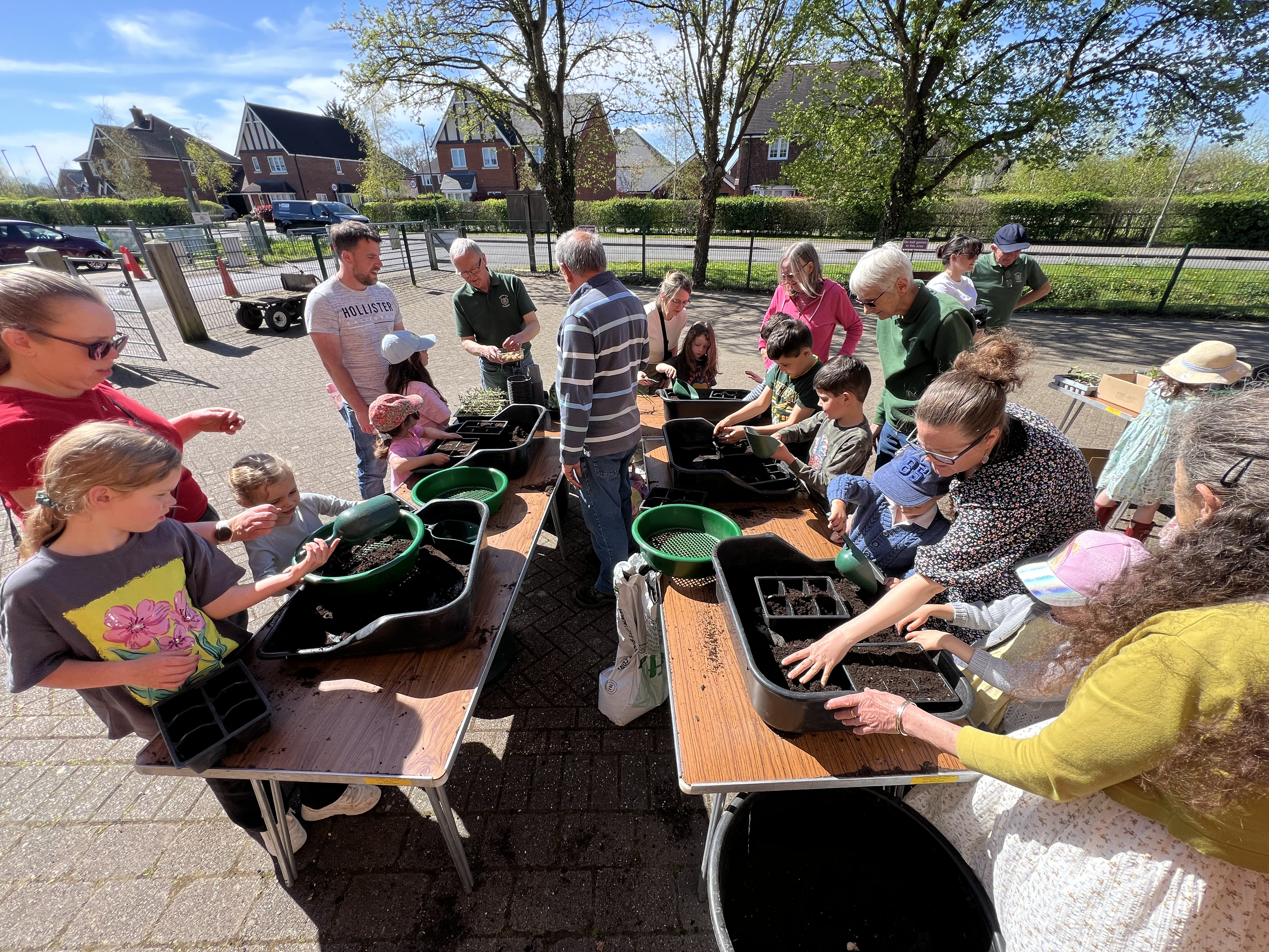 Children and adults gathered around a table sowing seeds in trays of soil.