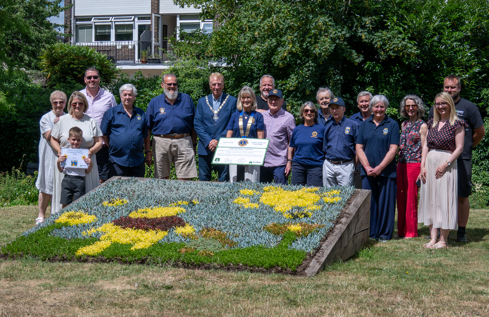 Group of people standing behind a raised flower bed showing an image of a yellow bear made from flowers.
