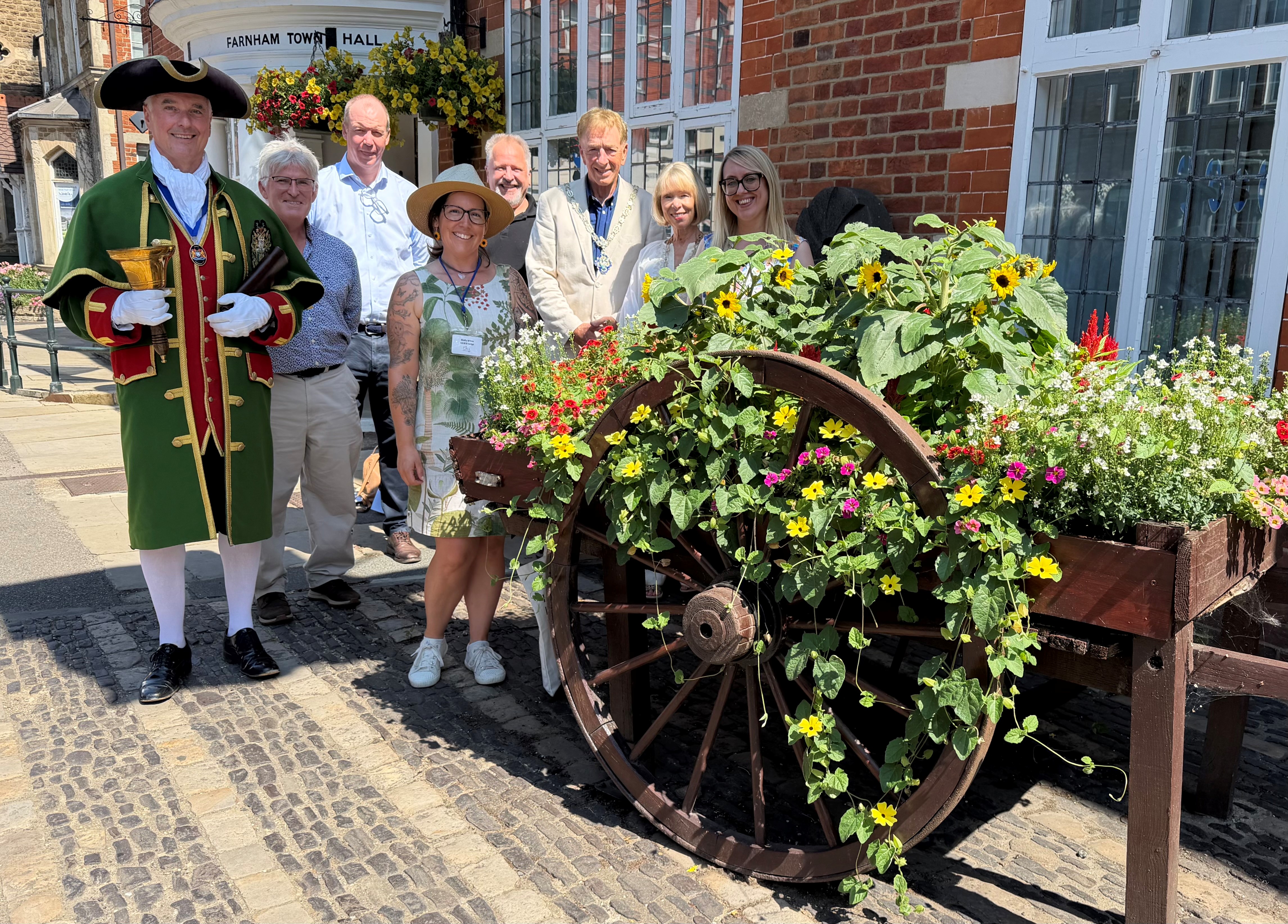 Group of people standing to the side of a hop cart planted with flowers.