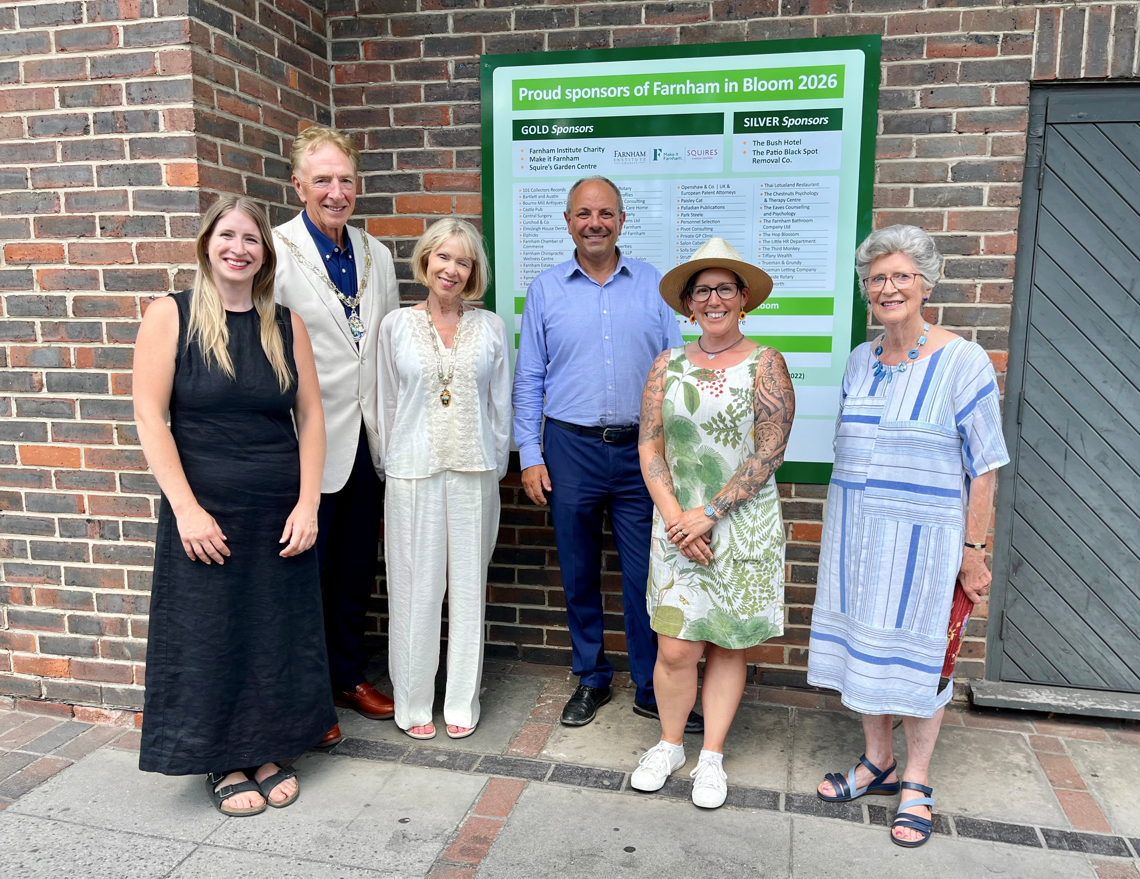 Group of people standing in front of sign mounted on a brick wall.