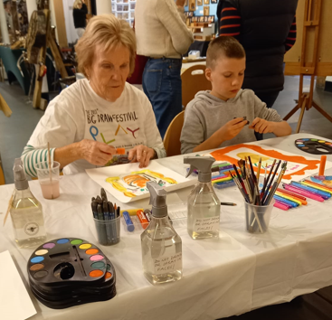Young boy and older lady sitting at a table drawing and painting pictures.