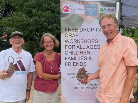 Three people standing in front of a banner advertising a craft workshop