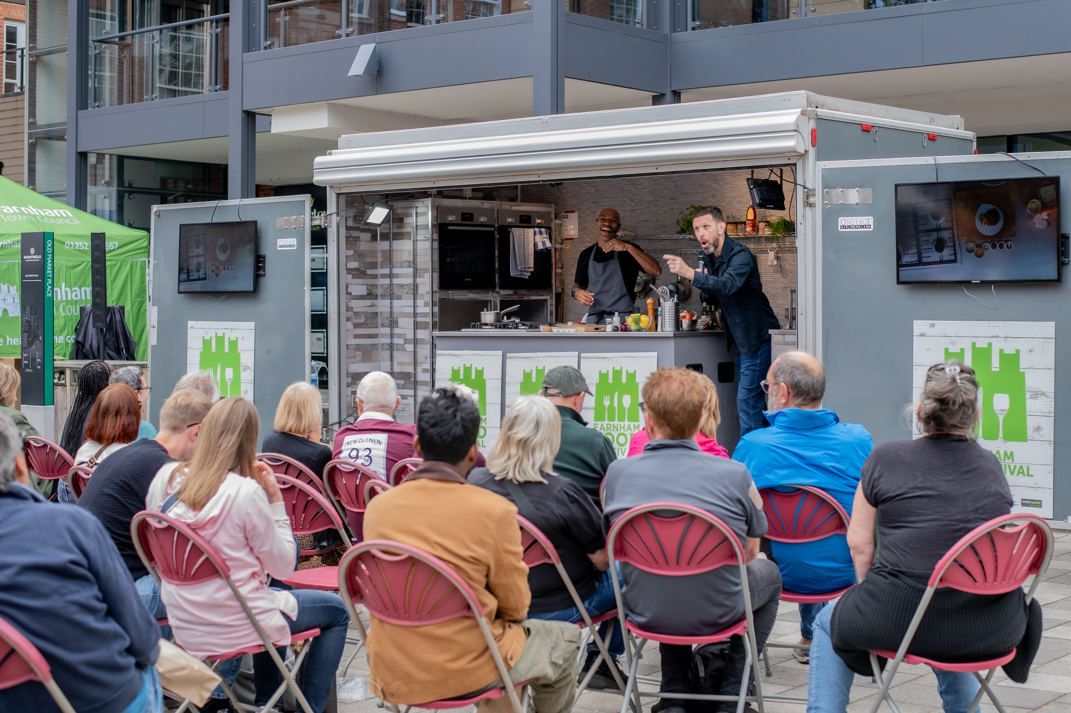 Crowd of people sitting down and listening to a man next to a food theatre.