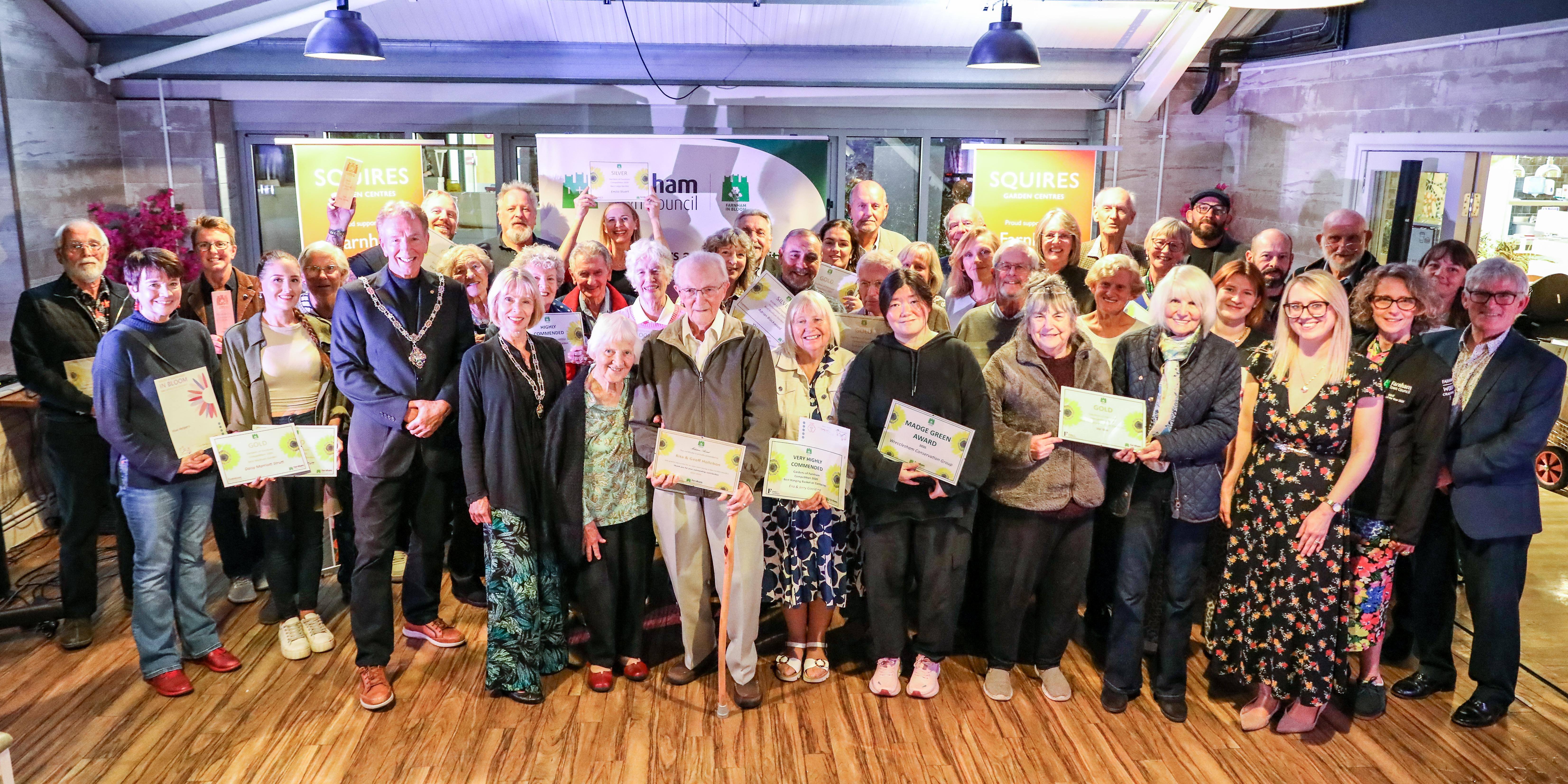 Large group of adults holding certificates and prizes.
