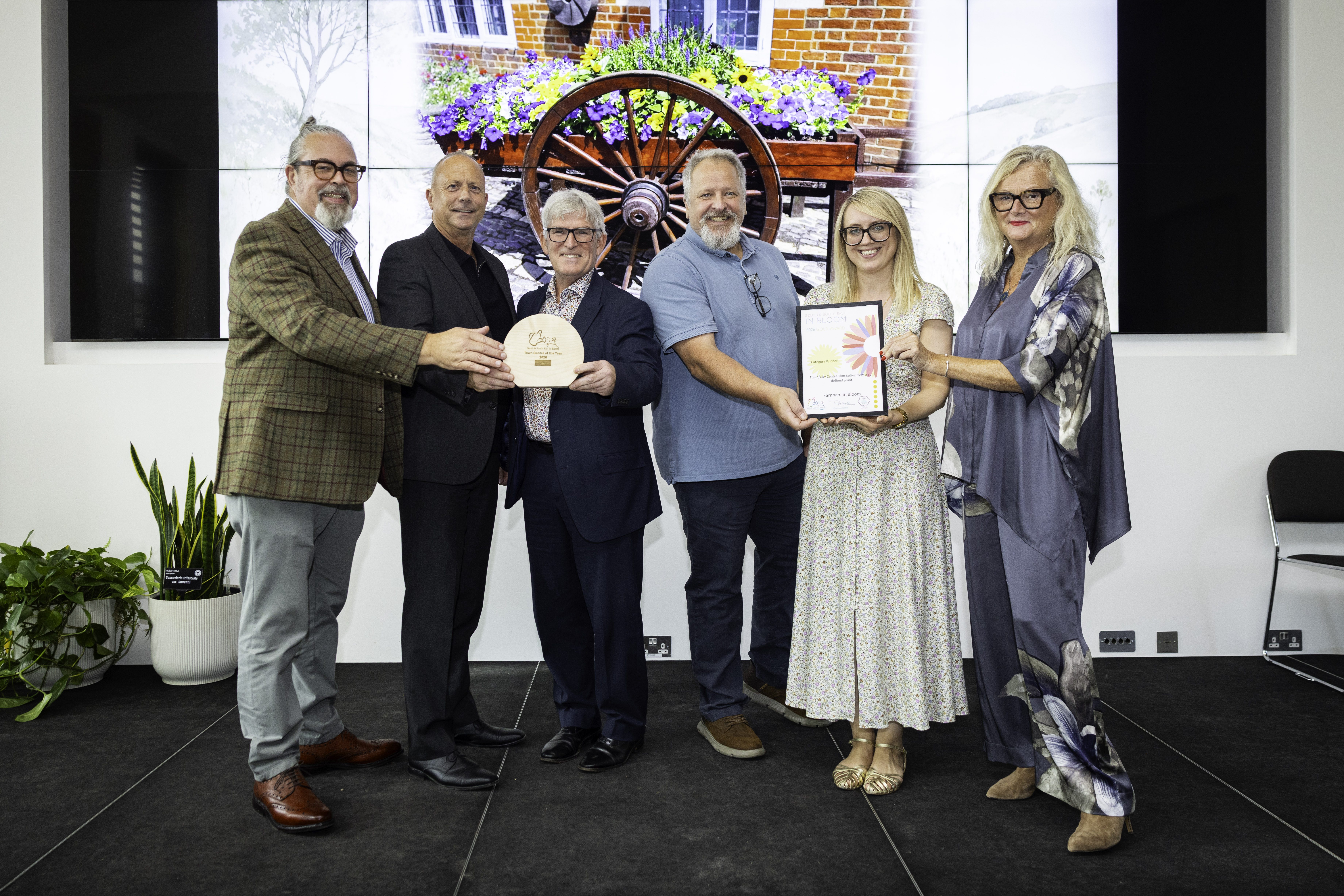 Six people standing in a row. One person is holding a certificate and one is holding a trophy.